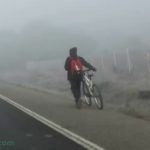 Peaton empuja ciclo en carretera con niebla